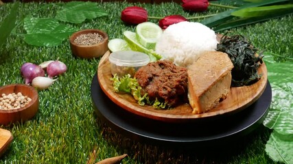 Wall Mural - Close up Padang Rice traditional food from Padang, Indonesia on a wooden plate, containing white rice, beef rendang, omelette, sliced ​​cucumber, green chili sauce and jackfruit vegetable.