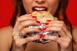 © Pixels Hunter - Woman with red nails holding and eating a sandwich wrapped in foil on a vibrant red background.