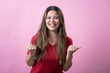 © Daniel - A happy young woman with long brown hair and light skin, wearing a red T-shirt, smiles brightly and clenches her fists in a celebratory and enthusiastic gesture against a pink background.
