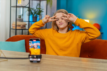 Caucasian teenager boy creating trendy selfie videos on smartphone at home. Performing dance moves while sitting on couch by table, engaging in social media content with enthusiasm and creativity