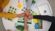 © kinomaster - Top view creative project team meeting in boardroom at desk, discussing ecological project, presenting visual concept graphics, making team fist bump hand gesture.