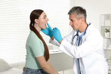 Wall Mural - Doctor examining woman's throat with tongue depressor in clinic