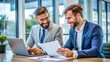 © engincan - Two busy happy diverse male employees checking documents talking in office. Professional young business man manager financial advisor consulting client having conversation sitting at work meeting.