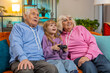 © Andrii Iemelianenko - Happy Caucasian grandparents and granddaughter using joystick controller playing videogame fun on sofa at home. Girl with senior man and woman enjoying success winning online game during weekend.