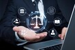 © Dream Stock - A close-up of a business professional's hand presenting a glowing holographic representation of justice and law symbols.