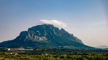  view of a single tall mountain with a rock facade in a rural area under a clear blue sky with one cloud