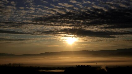 Wall Mural - time lapse orange sunrise behind a mountain in the valley with a sea of fog in the foreground