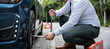 © sorapop - Asian young businessman unscrewing lug nuts on the wheel with a lug wrench. Handsome man wearing white shirt road assistance changing car wheel on the highway. Car mechanic changing car tyre concept.