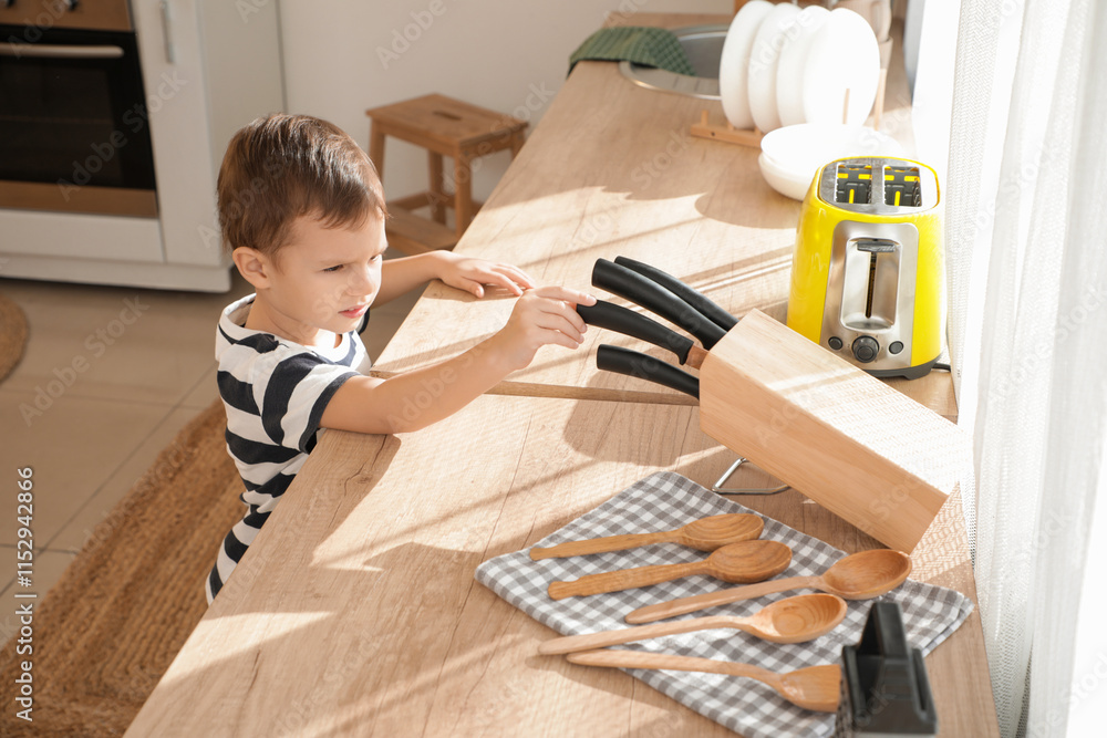 Cute little boy taking knife from counter in kitchen. Child at risk