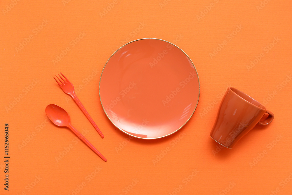 Cup, plate and cutlery on orange background