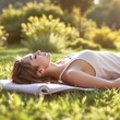 © TatChong - Serene young woman lying relaxed on yoga mat in grassy park sunbathing