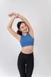 © bongkarn - A beautiful, healthy Asian woman in sportswear stretching her arms and body, studio background.