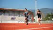 © bongkarn - Two determined Asian athletes running on a track in a stadium on a sunny day.