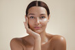 © Buyanskyy Production - Close-up of a woman with clear skin posing thoughtfully, resting her face on her hand against a light beige background. The background is a soft beige, accentuating her smooth skin and calm demeanor.