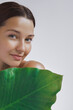 © Buyanskyy Production - A serene young woman with radiant skin holds a large green leaf, highlighting her connection to nature and natural beauty. Ideal for promoting eco-friendly skincare, wellness, and self-care concepts