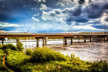 Wall Mural - A bridge spans a river with a cloudy sky in the background