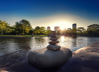 Poster - Serene sunset over a city skyline reflected in calm water.  A carefully balanced rock cairn sits on a large stone by the tranquil waters.  Peaceful, balanced, and beautiful.