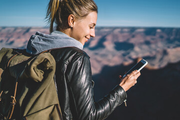 Wall Mural - Smiling female tourist with backpack blogging in networks using good mobile connection in arizona national park,hipster girl checking mail on smartphone hiking in wild nature carrying rucksack