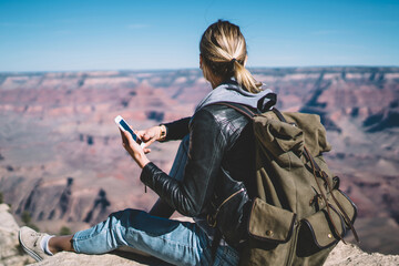 Wall Mural - rear view of female traveler checking connection on telephone sitting on high mountain hill, hipster