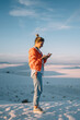 © BullRun - Full length of female traveler satisfied with good data connection sending messages on mobile phone during journey to White sands,hipster girl blogging via smartphone exploring desert in New Mexico
