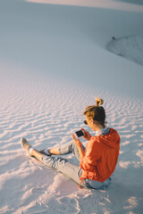 Wall Mural - female traveler sitting at white sands landscape with mobile phone sending messages ,hipster girl ch