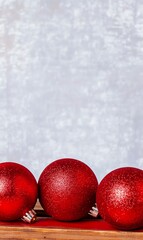 Wall Mural - Three red Christmas ornaments on wooden surface against a sparkly background.