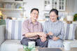 © ultramansk - A cheerful elderly couple sitting together on a cozy sofa, holding hands and smiling warmly. They enjoy their peaceful moments together, embodying love, companionship, and happiness in their home.