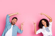 © deagreez - Excited couple pointing upwards against a pink colorful background expressing joy