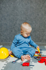 Wall Mural - Boy 1 year old in a blue romper plays with toys at home in the living room. Child self-development. Toys for babies.