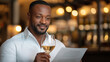 © Bonsales - Elegant gentleman sipping white wine, perusing restaurant menu in warm, intimate dining setting with refined culinary ambiance