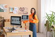 © Pixel-Shot - Young female graphic designer with laptop standing near her workspace in office