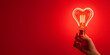 © Ekaterina - A vibrant red heart shaped light bulb glowing brightly in a hand, set against a deep red background, symbolizing love and passion