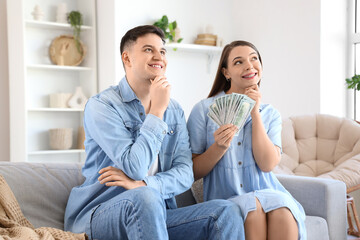 Wall Mural - Dreaming young couple with money sitting on sofa at home