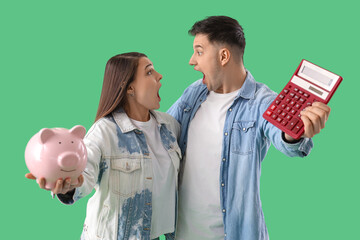 Wall Mural - Shocked young couple with piggy bank and calculator on green background