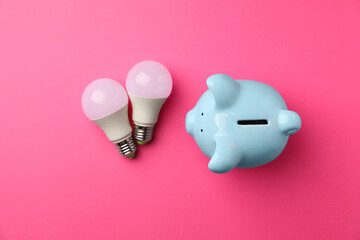 Wall Mural - Piggy bank and light bulbs on pink background, flat lay. Energy saving concept