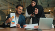 © Yuliia - Muslim team coworkers smile multiracial women man business partners male female businessman businesswomen hijab online chatting call video online conference discuss graphs documents negotiate office