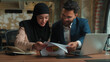 © Yuliia - Male female teamwork Arabian man muslim woman in hijab girl guy businessman businesswoman two happy business colleagues coworkers managers analyzing marketing graphs documents in office typing laptop