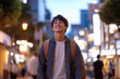 © romanets_v - Young asian male smiling on bustling city street at dusk