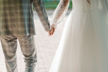 Wall Mural - A Romantic Moment of a Newlywed Couple Holding Hands in a Sunlit Outdoor Setting