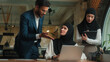 © Yuliia - Multiethnic coworkers business women man teamwork collaboration Muslim businesswomen in hijab Arabian businessman help with online laptop project mentor teach intern student consult in office company
