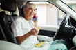 © Davor - Smiling senior nurse having phone call while eating healthy salad in car