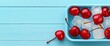 © HambaTuhanImages - Chilled cherries in a blue container on a light blue wooden background.