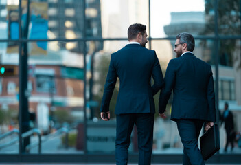 Wall Mural - Two businessmen in elegant business suit. Business center. Walking colleague. Colleague and friends. Two successful business men walking outdoor. Businessmen go to work. Business talking