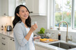 © KingKongThePitbull - Healthy beautiful asian woman holding glass of water and taking vitamin, taking Pill standing in modern kitchen - Smiling at camera