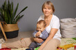 © sementsova321 - A grandmother comfortably holds her baby on the floor, surrounded by playful decorations and indoor plants. The warm atmosphere reflects a loving bond between them