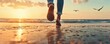 © Mnt - A person walking barefoot along the beach at sunset.