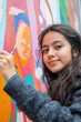 © Lakkhana - Close-up of a teenage Latina girl painting a mural about climate change, expressive and vibrant, urban wall backdrop,