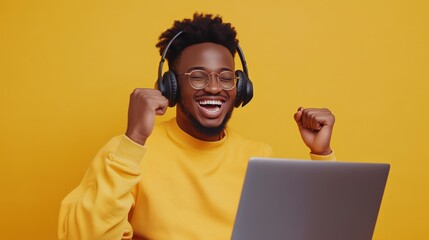 Wall Mural - a man in a yellow shirt is wearing headphones and smiling while using a laptop. concept of happiness