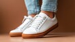 ©  Shomixer - Pair of classic white sneakers grounded on a warm brown floor, paired with light blue denim. The image conveys an understated elegance and relaxed fashion sense.
