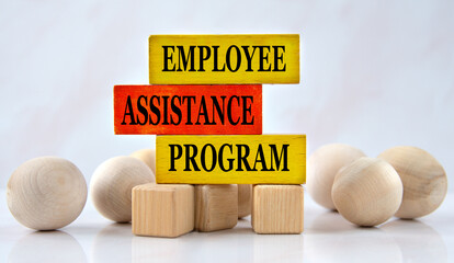 EMPLOYEE ASSISTANCE PROGRAM - words on a wooden brown block with balls lying next to it on a white background